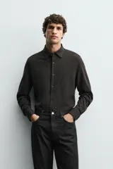 Camisa de corte relajado confeccionada en tejido de algodón con textura. Presenta cuello italiano, manga larga con puños abotonados y cierre frontal mediante botonadura.