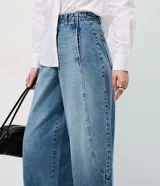 Pantalón de jean estilo barrel con cintura alta, cierre frontal con botón y cremallera, y recortes laterales que definen su silueta amplia y moderna.