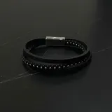 Pulsera para hombre de cuero negro, compuesta por tres tiras: una tira plana, una tira trenzada y una tira con cuentas metálicas. Cierre magnético plateado.