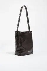 Bolso de hombro tipo tote de Bimba y Lola, confeccionado en piel vacuna con acabado brillante. Presenta un diseño estructurado con asa larga decorada con tachas metálicas plateadas y cierre de botón a presión.