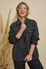 Campera de jean color negro con diseño de tachas metálicas plateadas distribuidas en el cuello, los bolsillos frontales y a lo largo de la parte delantera. Cuenta con cierre frontal de botones metálicos y mangas largas.