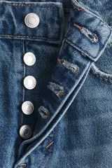 Jean tobillero de cinco bolsillos en denim de algodón rígido, con piernas rectas y cintura de tiro alto con cierre y botón. Presenta un lavado desgastado con sutiles roturas.