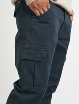 Pantalon cargo de corte recto en color verde militar, confeccionado en sarga de algodón con elastano. Presenta bolsillos laterales con fuelle y tapa, además de bolsillos traseros con cierre de botón.