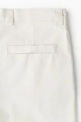 Pantalón sastrero de corte relajado en sarga color beige, con cierre y botón, bolsillos laterales y bolsillos traseros con botón oculto. Presenta piernas con pliegues.