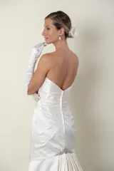 Vestido de novia largo color marfil, confeccionado en piel de ángel drapeada. Diseño strapless con apliques bordados en piedras en el escote, la cintura y la cola. Incluye guantes largos de satén blanco.