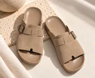 Sandalias planas de color beige con diseño de tira ancha en el empeine, hebilla metálica ajustable lateral y plantilla anatómica.
