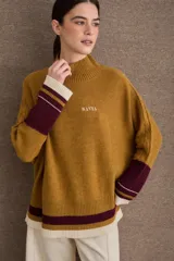 Buzo tejido de punto con silueta amplia, cuello alto y mangas largas. Presenta detalles de franjas en contraste en puños y ruedo, con tajos laterales y logo bordado en el pecho.