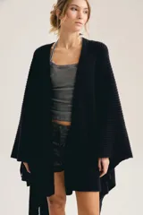 Poncho negro de punto grueso y diseño abierto tipo capa, con mangas amplias y ruedo asimétrico.