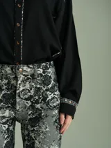 Camisa negra de algodón con mangas largas, cuello camisero y detalles de ribetes estampados a cuadros en los hombros, puños y aberturas de botones.