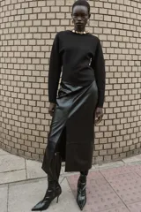 Jersey negro de cuello redondo con aplicación de bolas metálicas doradas, manga larga y bajo asimétrico. Cierre en la espalda con abertura y botón.