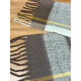 Bufanda rectangular de tejido grueso con diseño de cuadros en tonos azul, naranja, gris y beige, terminada con flecos en los extremos.