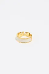 Anillo de latón con acabado dorado y diseño de logo calado. Presenta una banda ancha con detalles de esmalte blanco en los laterales.
