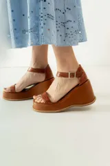 Sandalias negras de cuero sintético con plataforma y taco de cuña. Tienen dos tiras en el empeine y una tira con hebilla alrededor del tobillo.