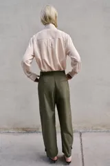 Pantalón de tiro alto en color verde militar, con corte barrel de pernera holgada que se estrecha hacia el tobillo. Presenta trabillas laterales ajustables en la cintura y en el bajo, bolsillos delanteros y cierre frontal con cremallera y botón.