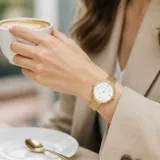Reloj analógico Mini Focus con caja redonda de metal dorado y malla de acero tipo milanesa. Esfera blanca minimalista con indicadores de hora en puntos dorados y movimiento de cuarzo japonés.
