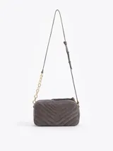 Bandolera de gamuza gris con diseño matelaseado en forma de V. Presenta un aplique metálico dorado en forma de labios en el frente y una correa combinada con cadena metálica dorada.
