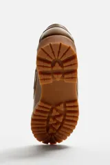 Zapato tipo náutico de cuero color marrón, con cordones, ojales metálicos laterales y suela de goma con volumen y relieve dentado.