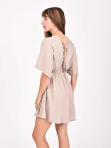 Monoprenda corta de color beige claro, con escote en V profundo, mangas cortas tipo kimono y cintura elástica fruncida.