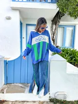 Sweater de punto azul con cuello polo blanco, diseño geométrico en el pecho en blanco y verde, y mangas largas.