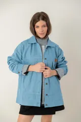 Campera de jean oversize color azul claro, con cuello camisero, cierre frontal con botones y bolsillos frontales. Presenta un diseño de corte amplio y cómodo con mangas largas.