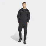 Campera deportiva Adidas del Real Madrid, color negro, con cierre frontal, capucha y corte entallado. Presenta el logo de Adidas y el escudo del club en tono sobre tono en el pecho.