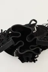 Cartera tipo bandolera de cuero gamuzado color marrón, con diseño de flecos laterales y detalle de tachas metálicas. Cuenta con cierre de cordón ajustable con borlas y correa regulable.