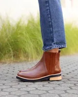 Botinetas de cuero color marrón con diseño de paneles combinados, incluyendo una sección lateral con textura grabada. Presenta una suela plana con detalle de madera y base de goma negra.