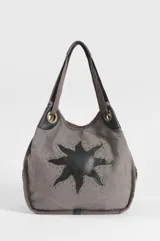 Bolso oversize de canvas color gris, con diseño de sol negro en aplique de cuero sintético y tachas metálicas decorativas. Cuenta con asas de hombro y argollas metálicas.