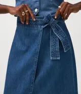 Pollera midi de jeans con diseño de traslape frontal, confeccionada en algodón. Presenta un corte tipo lápiz con cintura elástica y lazo ajustable del mismo tejido.