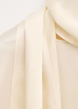 Blusa de seda color crema con cuello alto y detalle de pañuelo integrado en el escote. Presenta un diseño fluido y elegante de manga larga.
