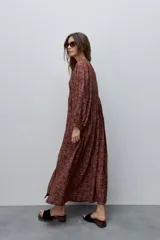 Vestido largo de silueta amplia y caída fluida, con estampado y recortes fruncidos que aportan movimiento. Presenta escote con abertura, cierre frontal con botones y mangas largas de volumen amplio con puños elastizados.