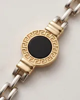 Pulsera de plata y lámina de oro 18k, con eslabones de cadena y un dije central redondo con piedra ónix negra y diseño de guarda griega.