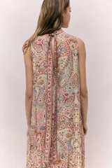 Vestido largo sin mangas, con cuello alto y abertura en la nuca. Presenta un estampado paisley en tonos tierra, rosados y celestes, con frunces a la altura de la cadera que generan una falda acampanada con vuelo.