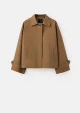 Chaqueta corta de algodón color marrón tostado, con cuello alto, cierre frontal de botones, bolsillos ribeteados y mangas largas con trabillas ajustables en los puños.