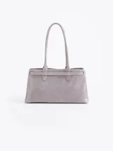 Cartera de hombro color gris, confeccionada en cuero vacuno descarne. Presenta un diseño estructurado con cierre de torniquete metálico y detalle de llavero colgante con candado y llave. Cuenta con doble asa fija.
