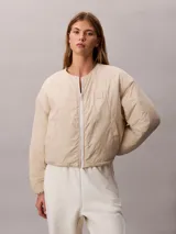 Campera puffer Calvin Klein color beige, de cuello redondo, manga larga y cierre frontal con cremallera blanca. Presenta bolsillos laterales y un parche con logo bordado en el pecho.