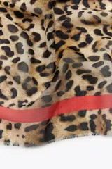 Pañuelo confeccionado en mezcla de modal y seda con estampado de leopardo en tonos marrones y beige. Presenta una franja lateral en color rojo a contraste y terminaciones deshilachadas.