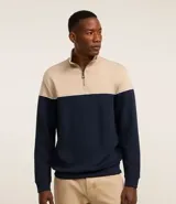 Buzo de media malla con diseño de bloques de color, presentando la parte superior en beige y la inferior en azul marino, separadas por una línea blanca. Cuenta con cuello alto con cierre frontal parcial y puños acanalados.