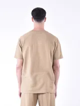 Remera de textura acanalada color tostado, con cuello redondo y cierre frontal parcial con botones. Presenta un bolsillo pequeño en el pecho con detalle de logo.