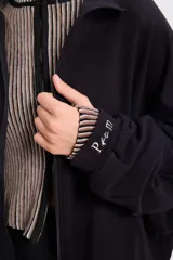 Campera holgada de felpa color gris, con cuello alto, cierre frontal completo, mangas tipo murciélago y bolsillos laterales.