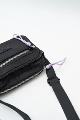 Cartera tipo bandolera de nylon color lila, con cierre frontal y correa ajustable negra.