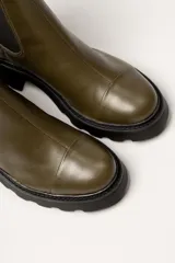 Bota tipo Chelsea de cuero color verde oliva, con paneles laterales elásticos negros y suela track de goma negra con taco cuadrado.