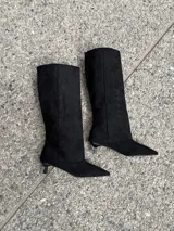 Botas altas de caña ancha en símil gamuza color negro, con diseño de punta fina y tacón fino bajo tipo kitten heel.