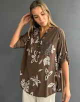 Blusa de corte holgado color chocolate con estampado floral en tonos claros. Presenta cuello camisero con tapeta frontal decorada con lentejuelas y un bolsillo en el pecho también con aplique de lentejuelas. Posee mangas tres cuartos con detalle de trabilla para arremangar.