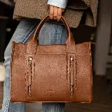 Cartera de cuero color tostado, estructurada, con doble asa de mano, correa desmontable y dos bolsillos frontales verticales con cierre. Presenta detalles de costuras pespunteadas y el logo de la marca grabado en la parte inferior.