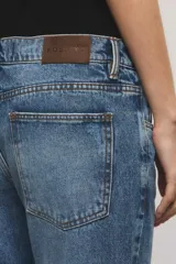 Jeans bootcut de tiro medio color azul, confeccionados en 100% algodón sin elasticidad, con sutiles roturas localizadas y diseño de pernera ensanchada desde la rodilla.