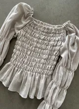 Blusa beige con cuerpo fruncido tipo nido de abeja, escote cuadrado y mangas largas abullonadas con puños elásticos.