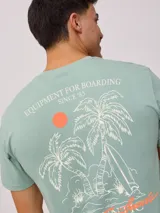 Remera negra de algodón con estampado en la espalda con palmeras, tabla de surf y texto en color blanco y fucsia.