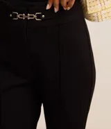 Pantalón de corte flare confeccionado en tejido punto roma, con ajuste ceñido en caderas y muslos, y apertura acampanada desde la rodilla. Presenta detalle decorativo metálico en la cintura y cierre frontal.
