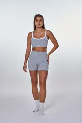 Conjunto deportivo compuesto por un top y un short de tiro alto en color gris. El top presenta breteles blancos, escote redondo y el logo de la marca estampado en el frente. El short cuenta con costuras decorativas blancas que realzan el diseño.